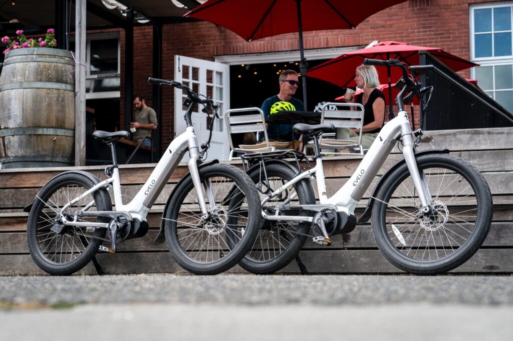 a pair of white electric bikes parked near couple sitting outside a restaurant